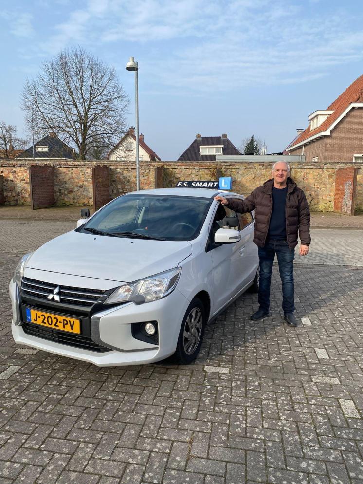 Instructeur van Rijschool F.S. Smart naast de witte Mitsubishi Space Star lesauto in Winschoten.